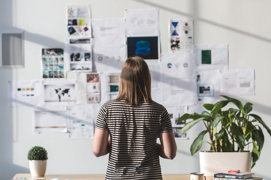 A woman stands in front of a wall of inspiration. Getting creative ideas can come from many places and this workspace is clearly full of brainstorms, inspirational walls and ideas ready to come to life. | LunaSola Designs